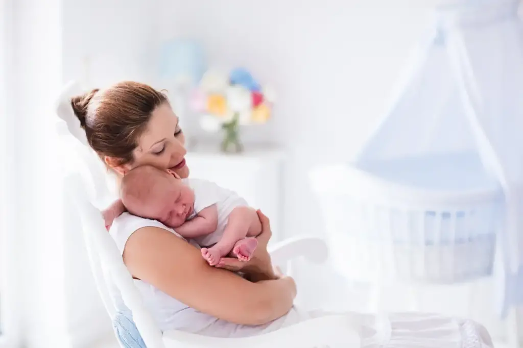 Mother Holding Her Baby Inside A White Painted Nursery Room